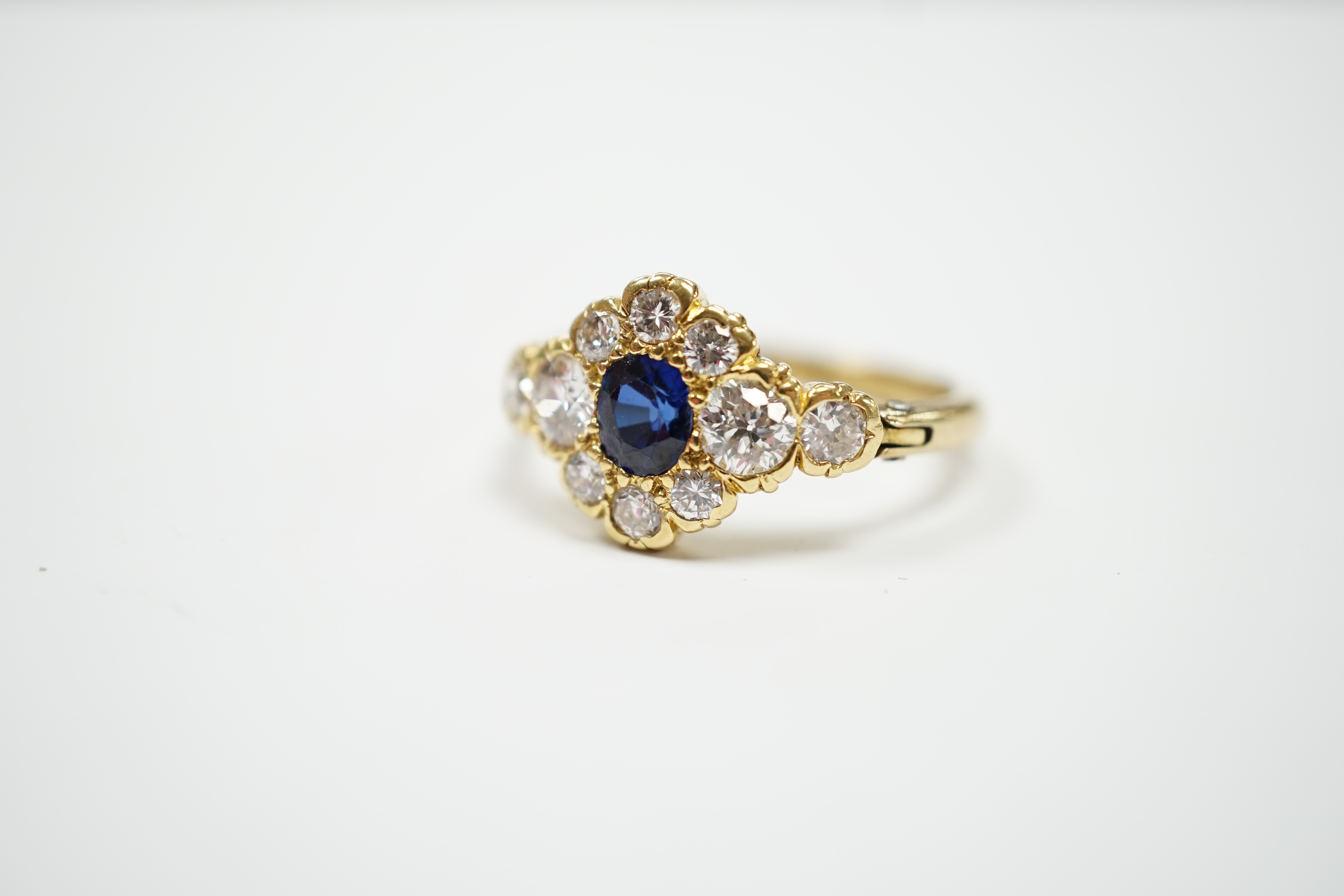 A modern yellow metal, synthetic sapphire and diamond set flower head cluster ring, with hinged shank, size U, gross weight 5.1 grams.